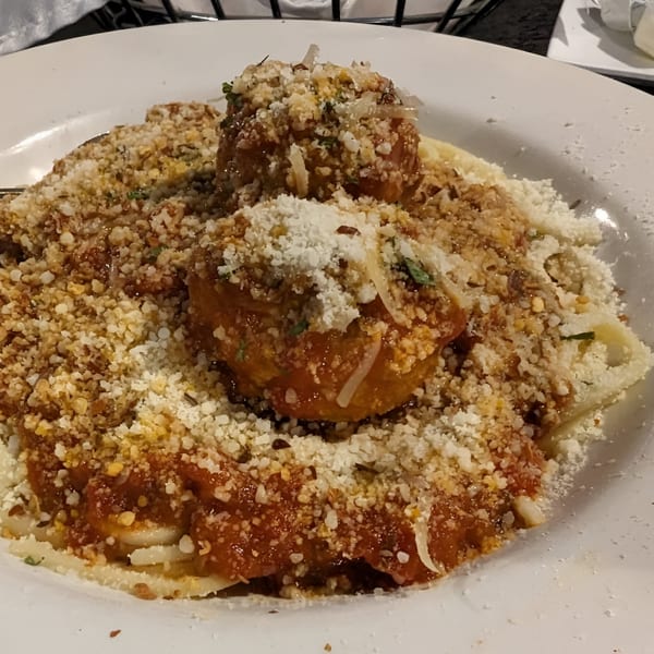Two large meatballs covered in red sauce, parmesan, and breadcrumbs on a bed of pasta.