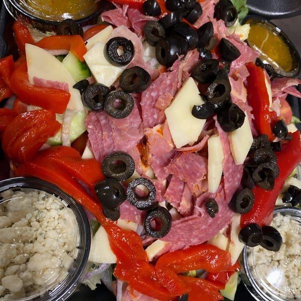 Close-up of a vibrant Italian salad with salami, cheese, red peppers, and black olives.