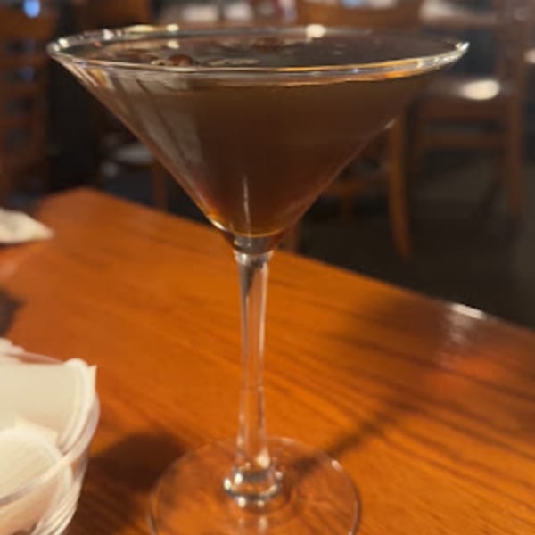A dark brown cocktail in a martini glass sits on a wooden table at Mona Lisas Ristorante.