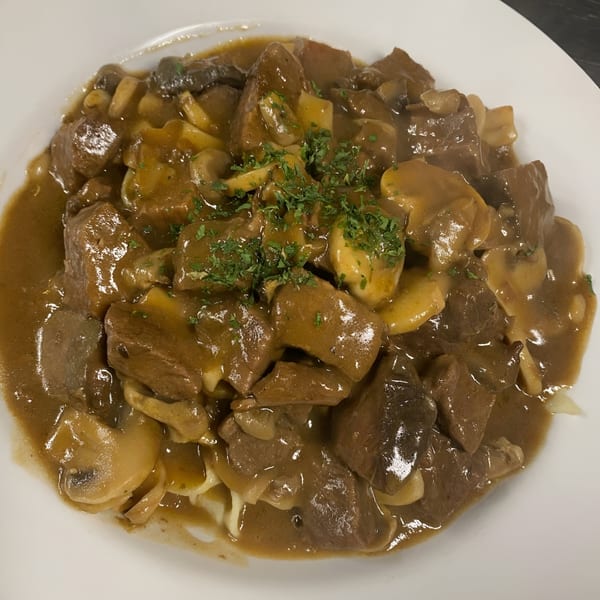 Mona Lisas Ristorante's beef and mushroom stew, garnished with parsley, served on a white plate.