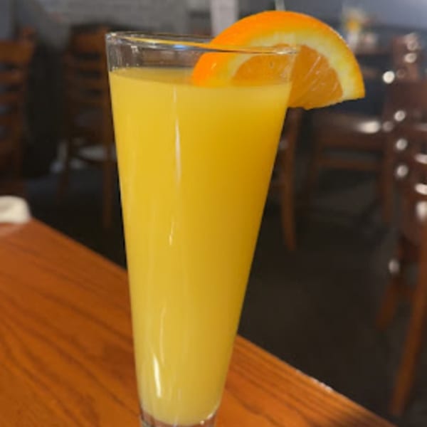 A tall glass of orange juice with an orange slice garnish on a wooden table.