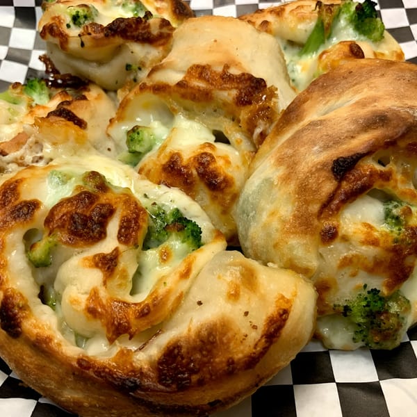 Close-up of baked Italian broccoli and cheese pinwheels with golden crusts on a checkered paper.
